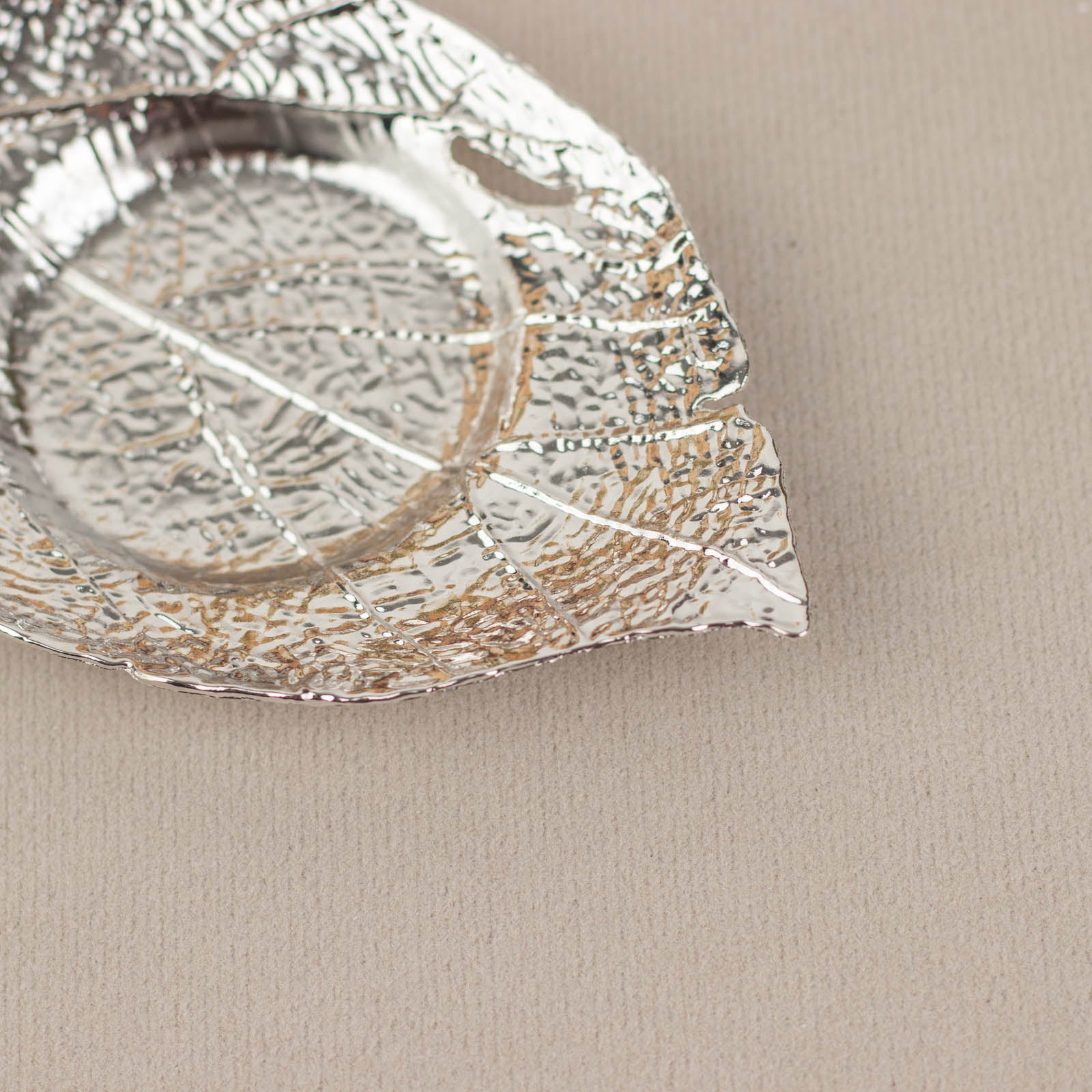 Shiny silver metal maple leaf tealight candle holder on beige background.