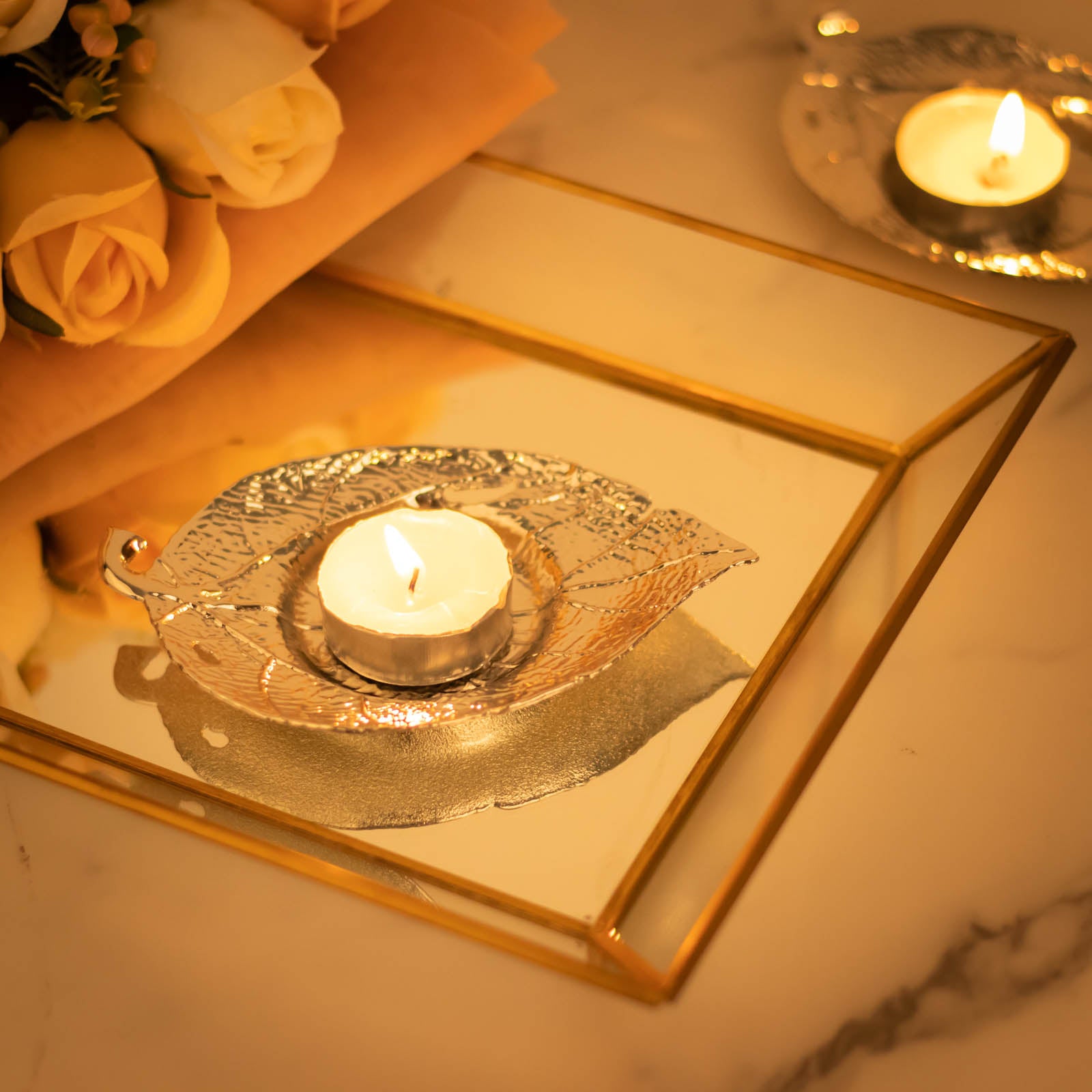 Shiny silver metal maple leaf tealight candle holders on a reflective surface.