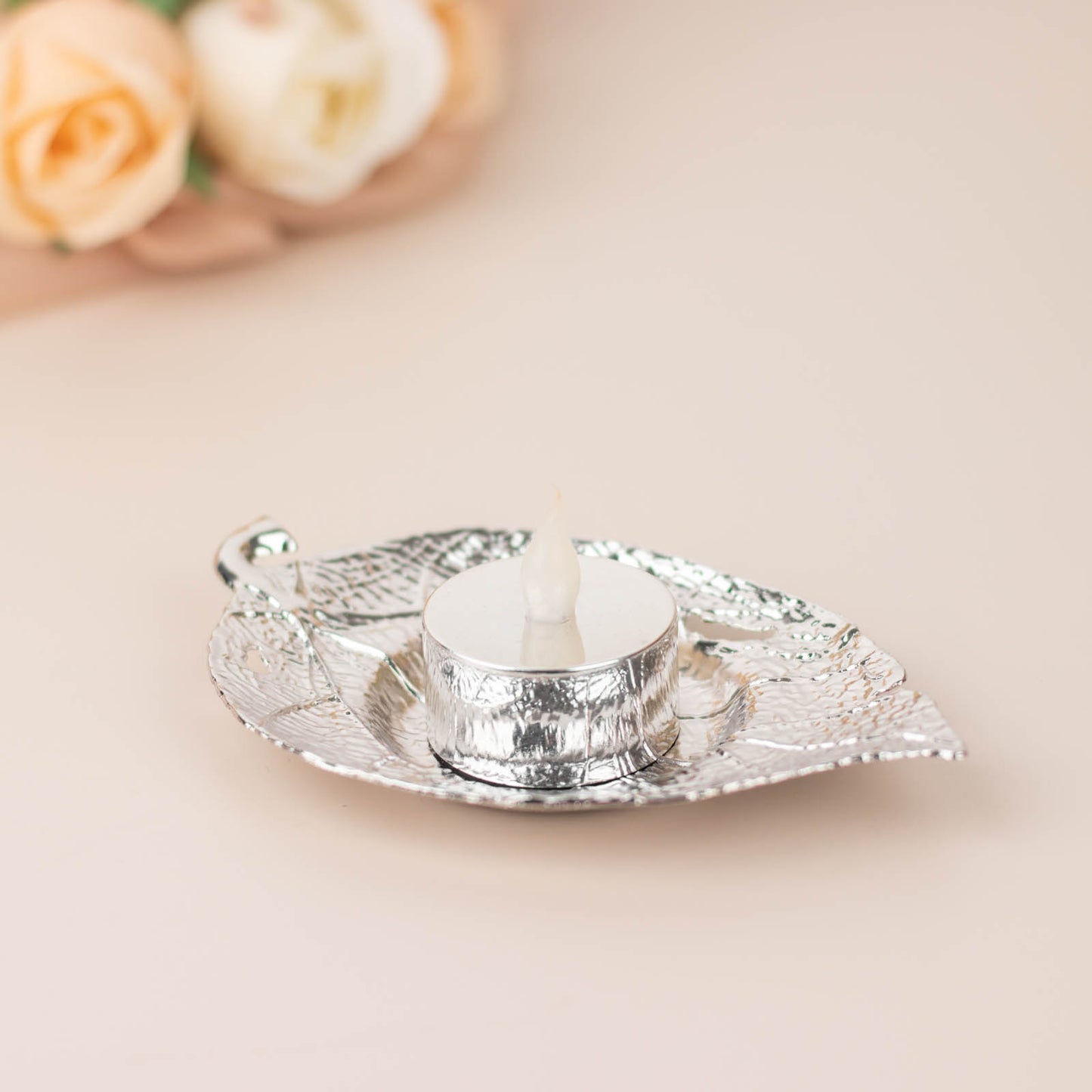 Shiny silver metal maple leaf tealight candle holder on a saucer.