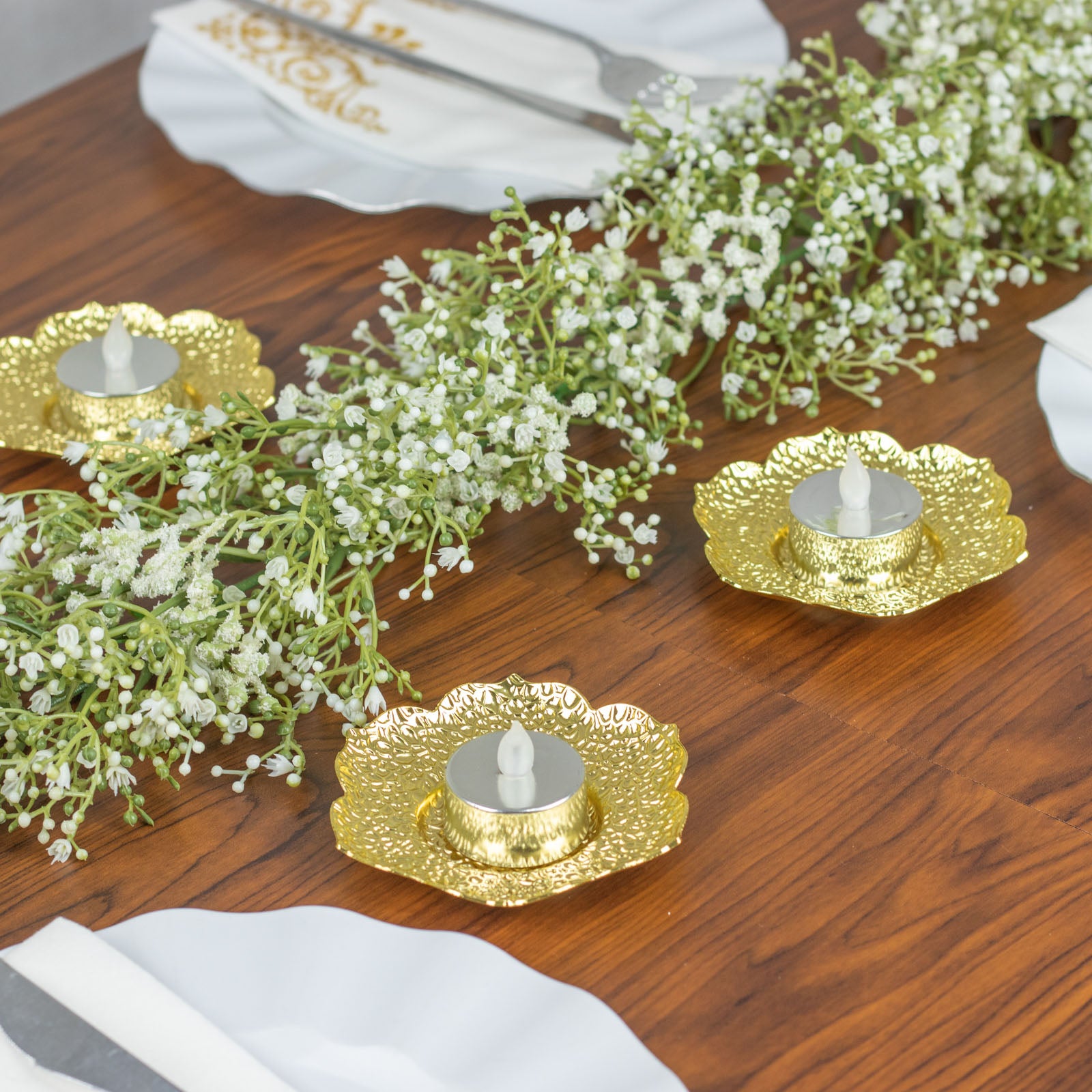 Shiny gold metal plum blossom tealight candle holders on a wooden table.