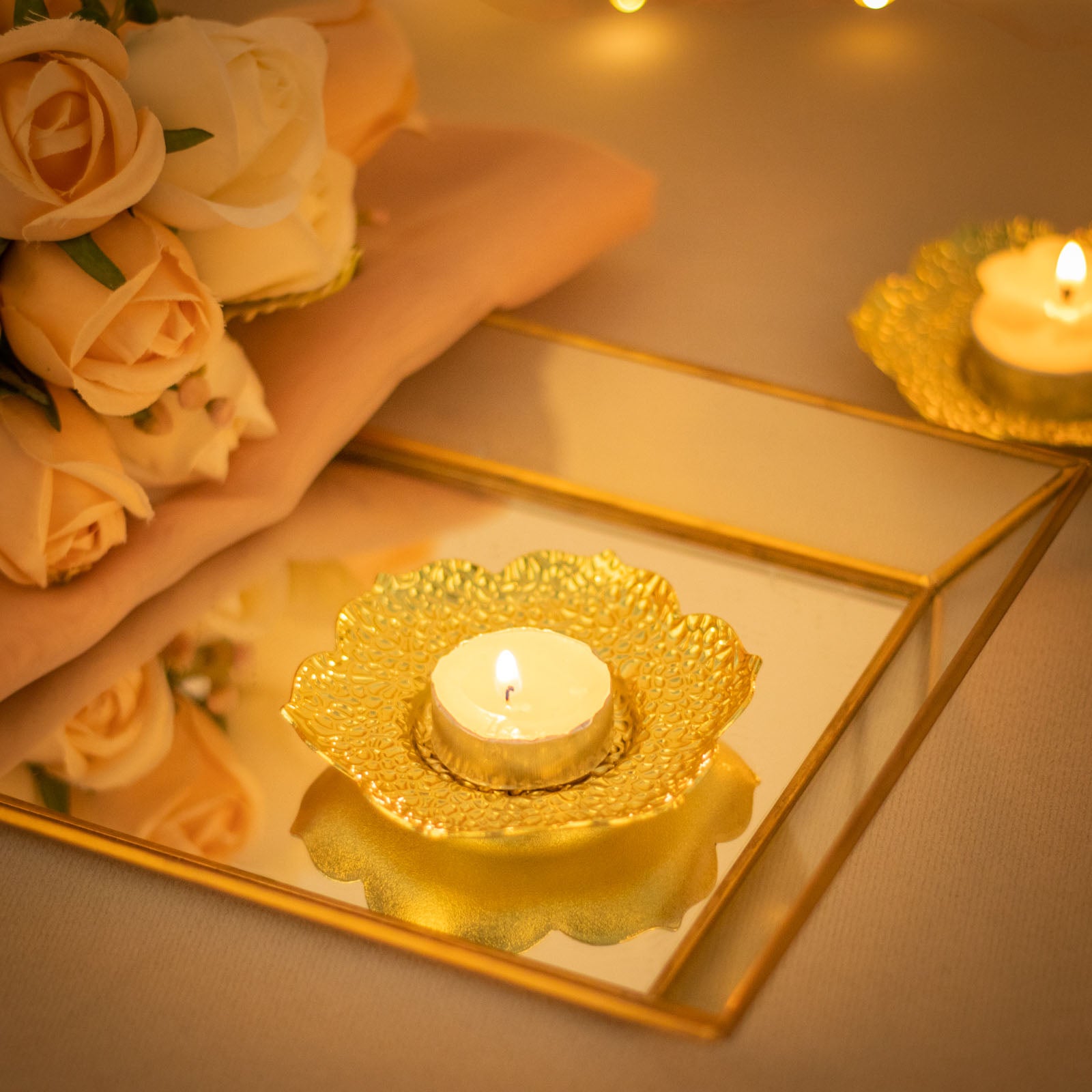 Shiny gold metal plum blossom tealight candle holder on a mirrored surface.