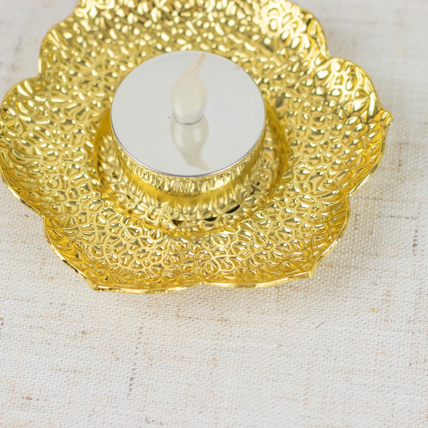 Shiny gold metal plum blossom tealight candle holder on a decorative saucer.