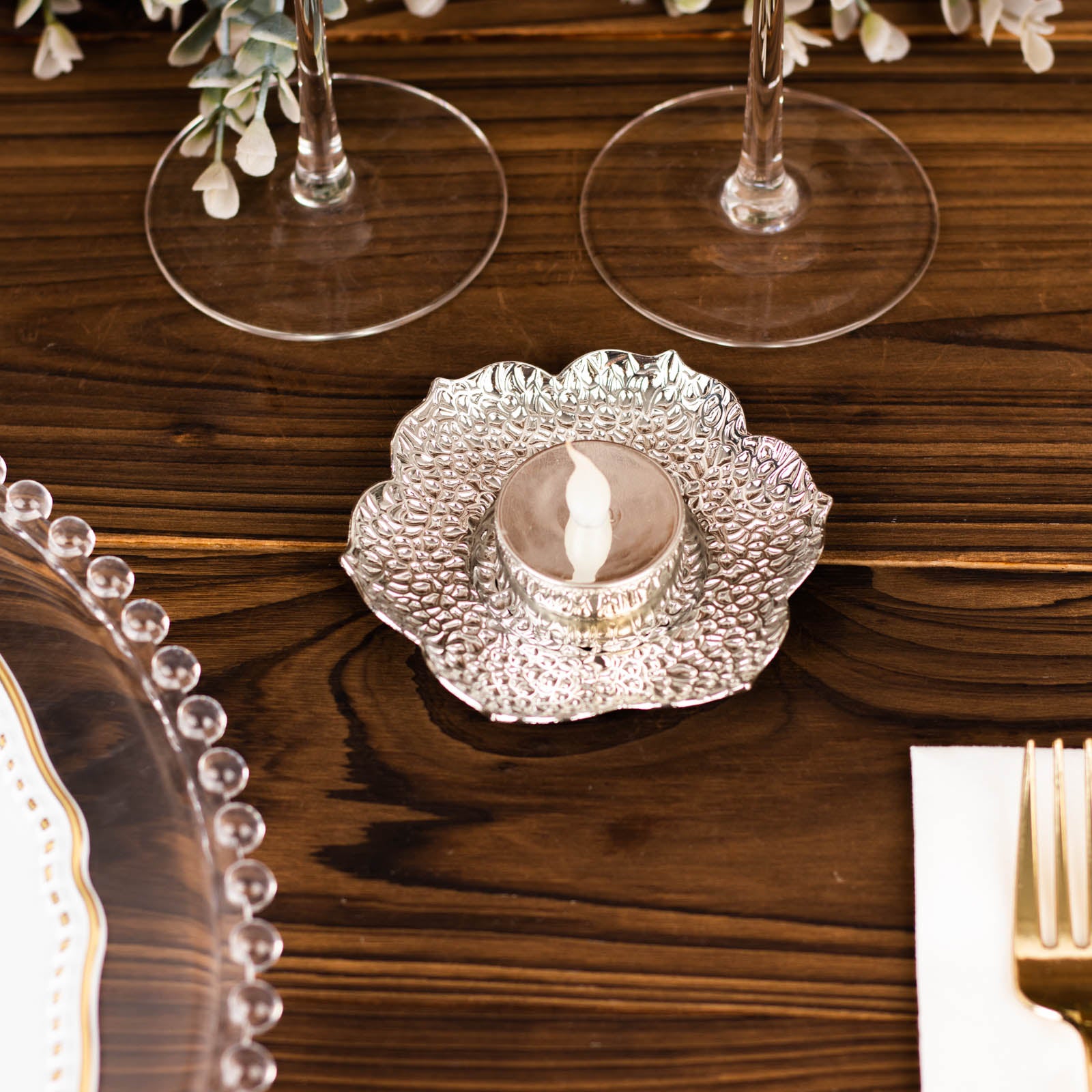Shiny silver metal plum blossom tealight candle holder on a wooden table.