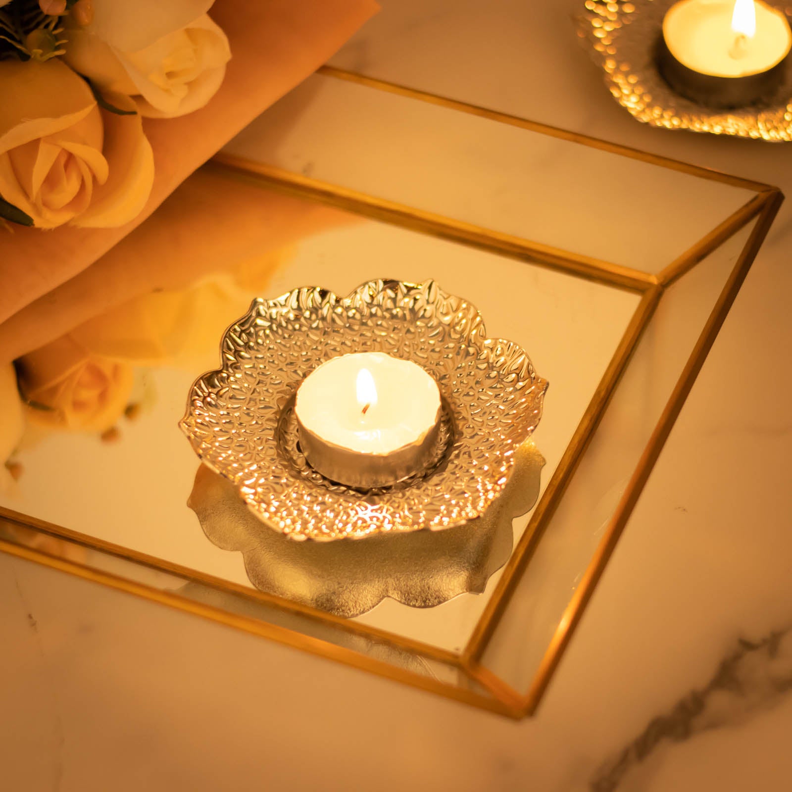 Shiny silver metal plum blossom tealight candle holder on a reflective surface.