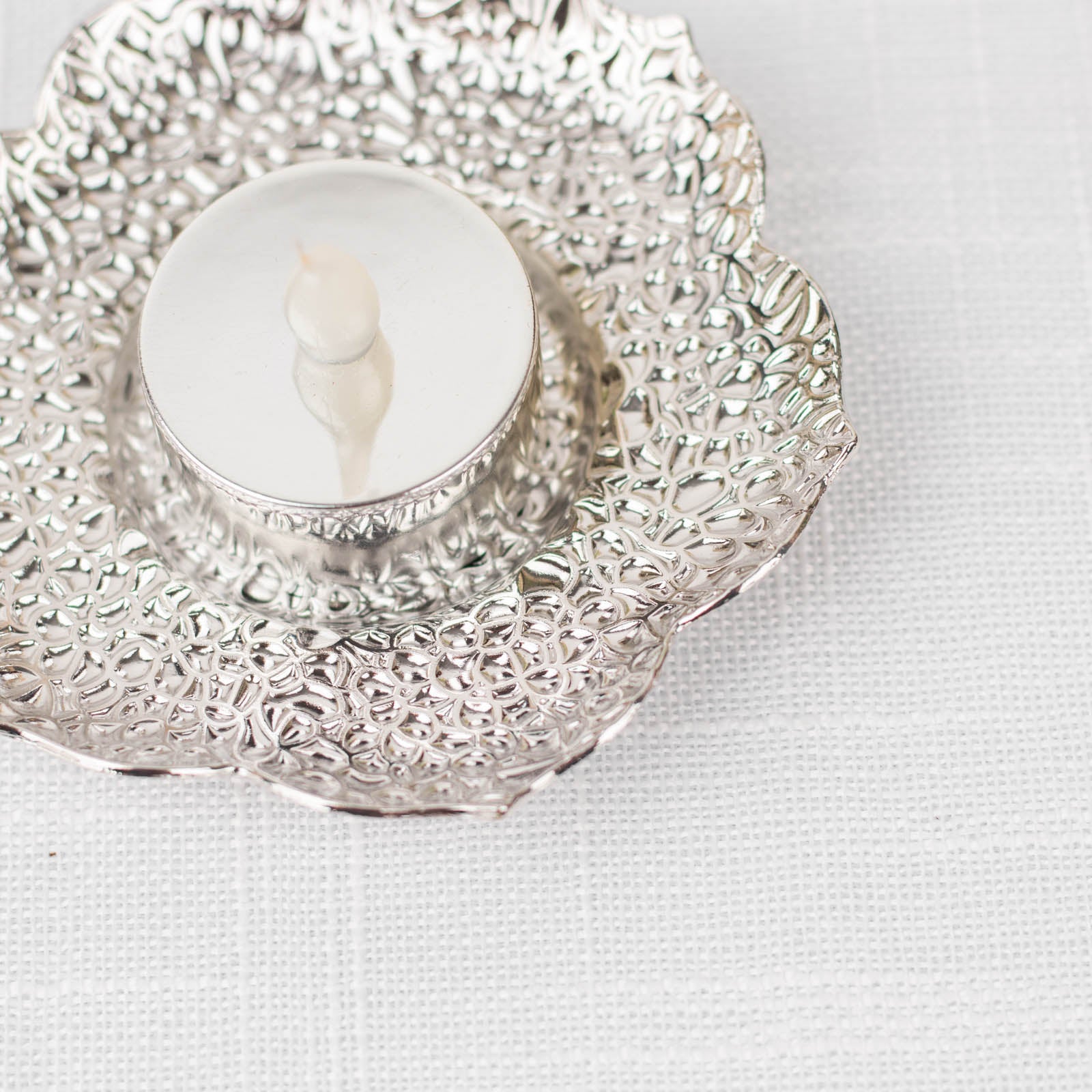 Shiny silver metal plum blossom tealight candle holder on white background.