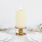 Gold metal candle holder with a white pillar candle, surrounded by decorative plates.