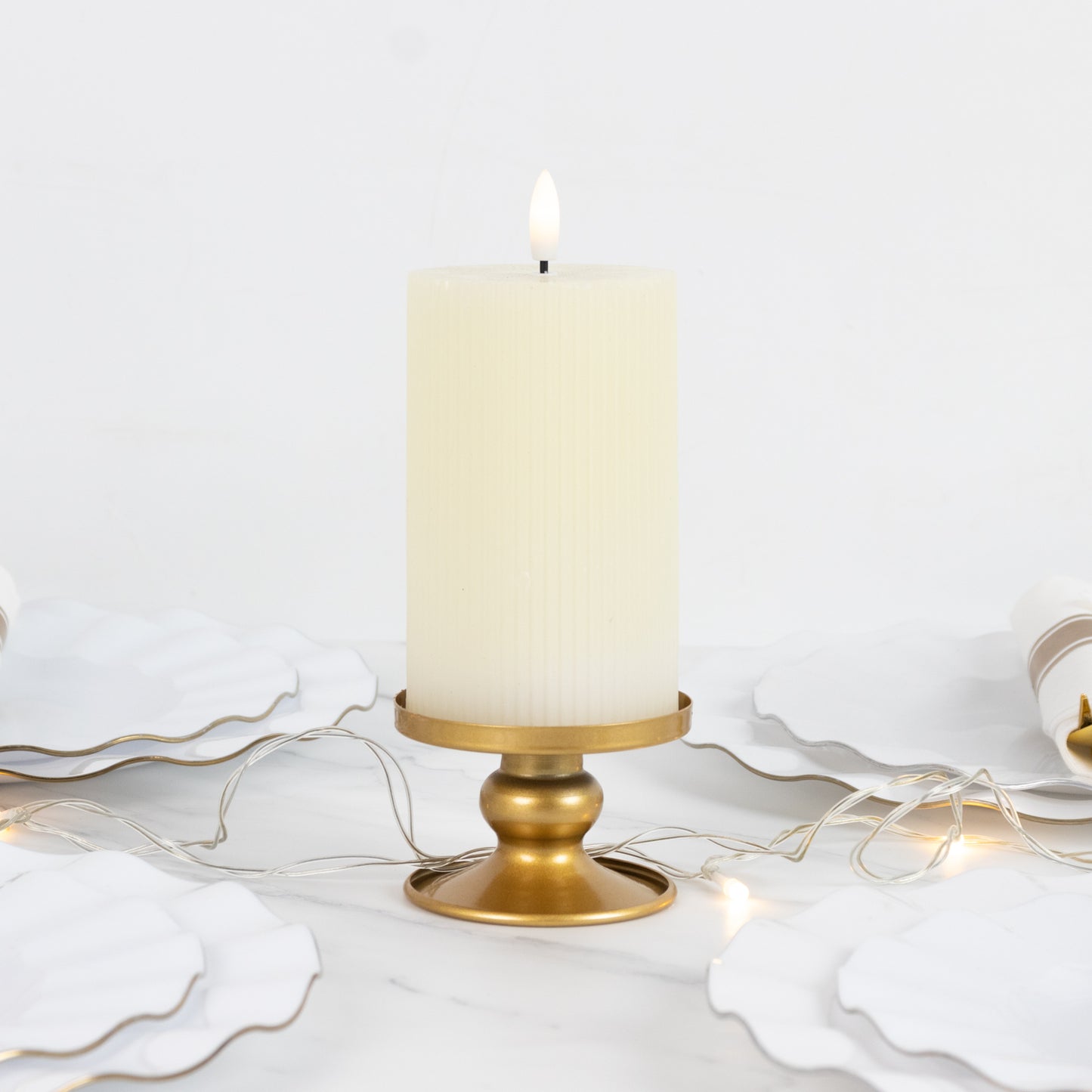 Gold metal candle holder with a white pillar candle, surrounded by decorative plates.