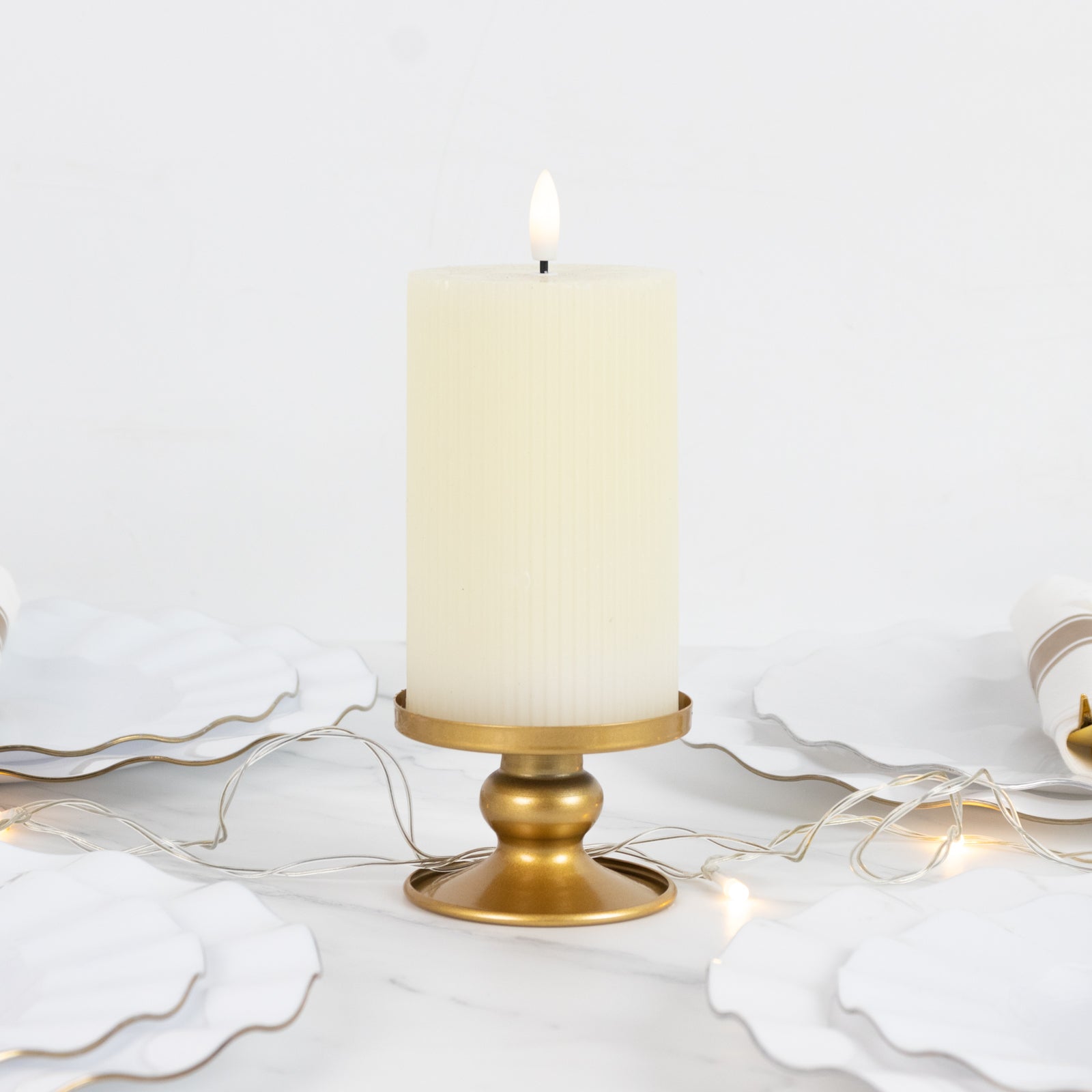 Gold metal candle holder with a white pillar candle, surrounded by decorative plates.