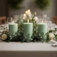 Sage green dripless pillar candles with smokeless wicks on a table centerpiece.