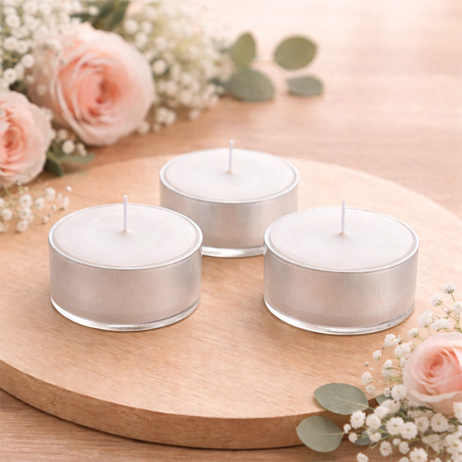 White tealight candles on a wooden surface surrounded by flowers.
