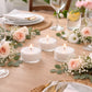 White tealight candles on a dining table with flowers and greenery.