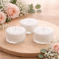 White tealight candles in clear cups on a wooden surface with flowers.