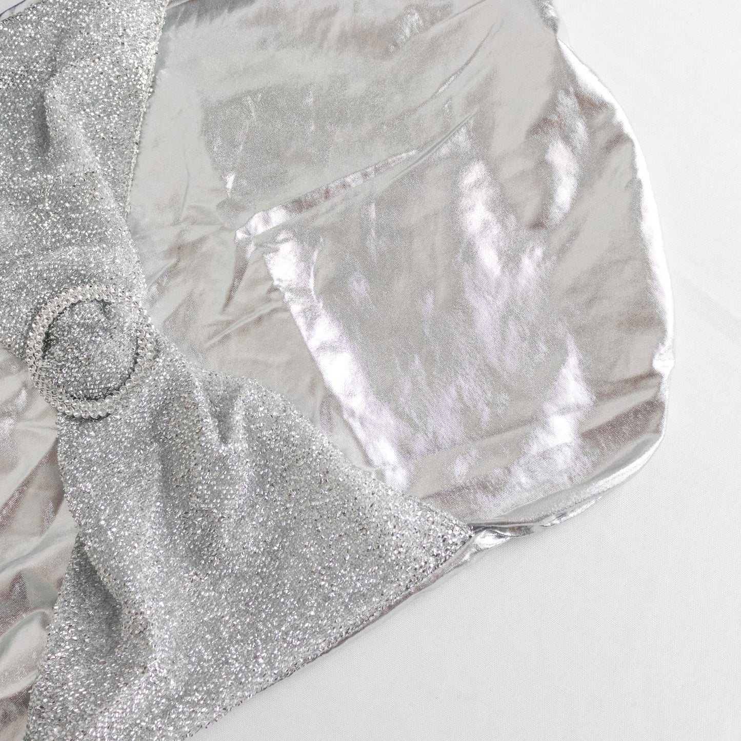 Metallic silver shimmer tinsel spandex chair cover with attached sash and rhinestone buckle.