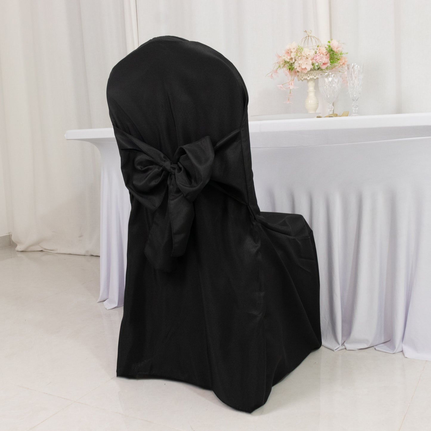 Black slip-on banquet chair cover with attached sash for event decor.