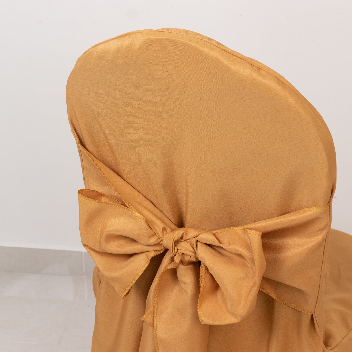 Gold polyester banquet chair cover with attached sash.