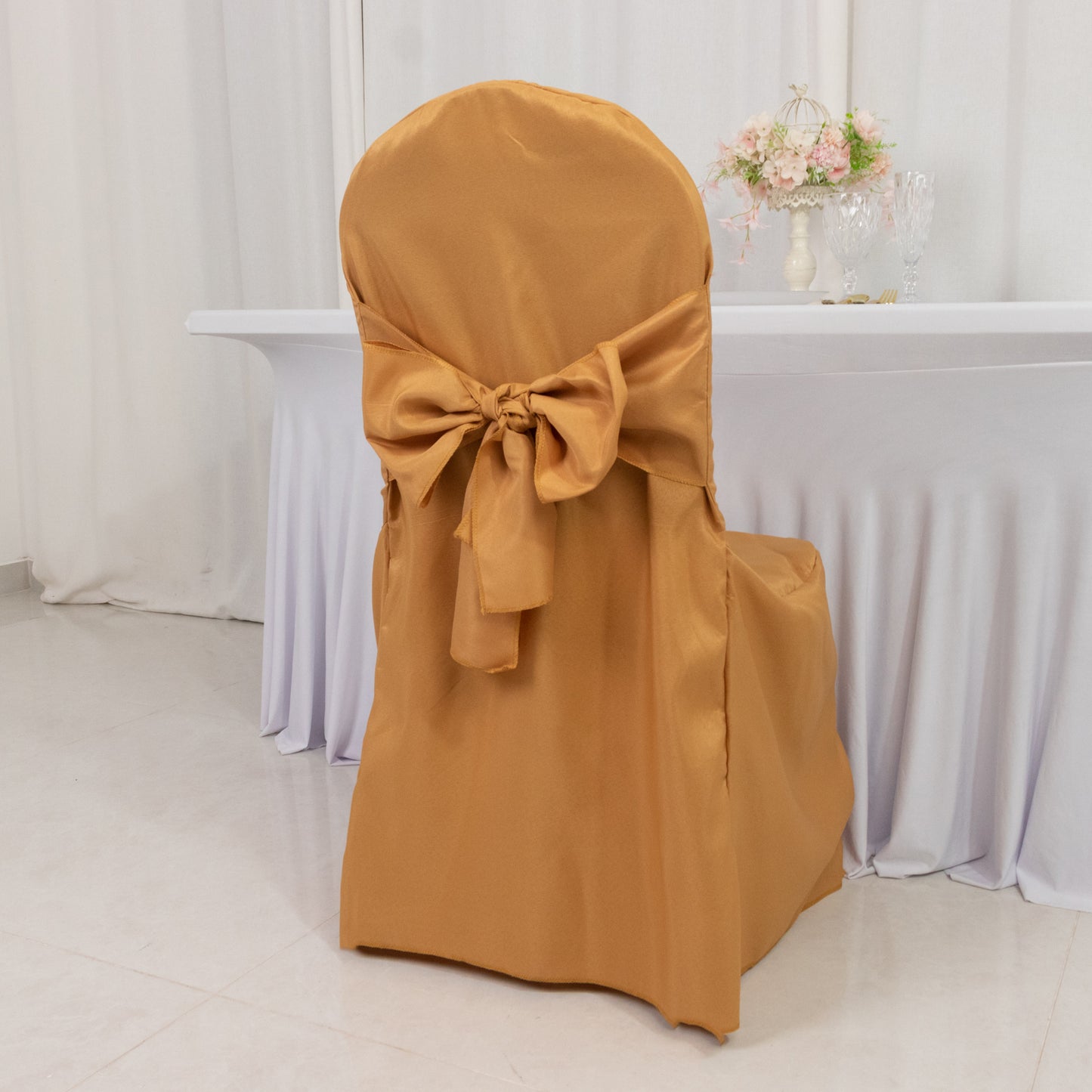 Gold banquet chair cover with attached sash for wedding decor.