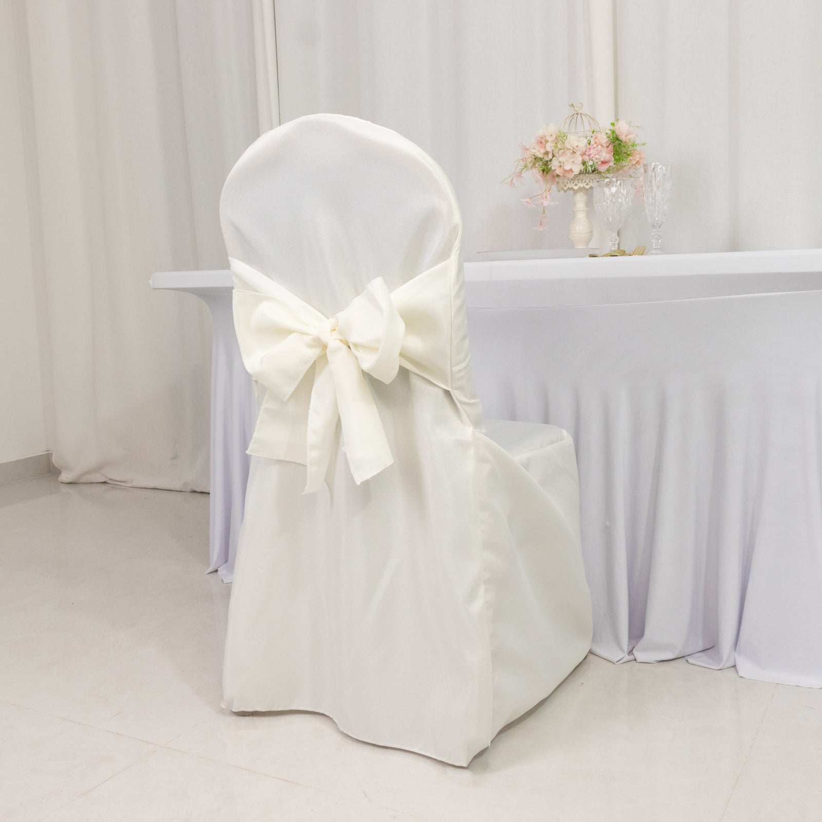 Ivory slip-on banquet chair cover with attached sash for event decor.