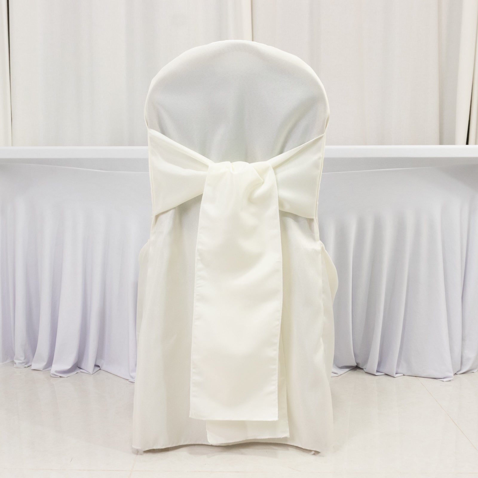 Ivory slip-on banquet chair cover with attached sash for events and weddings.