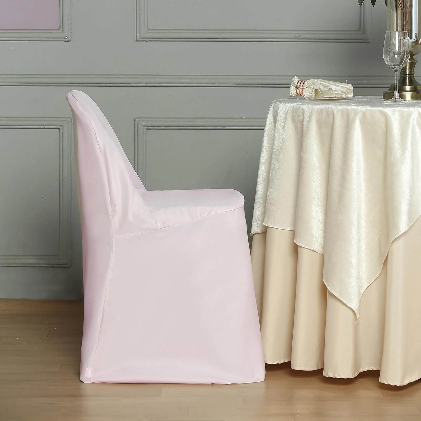 Blush polyester folding chair cover on a chair next to a table.