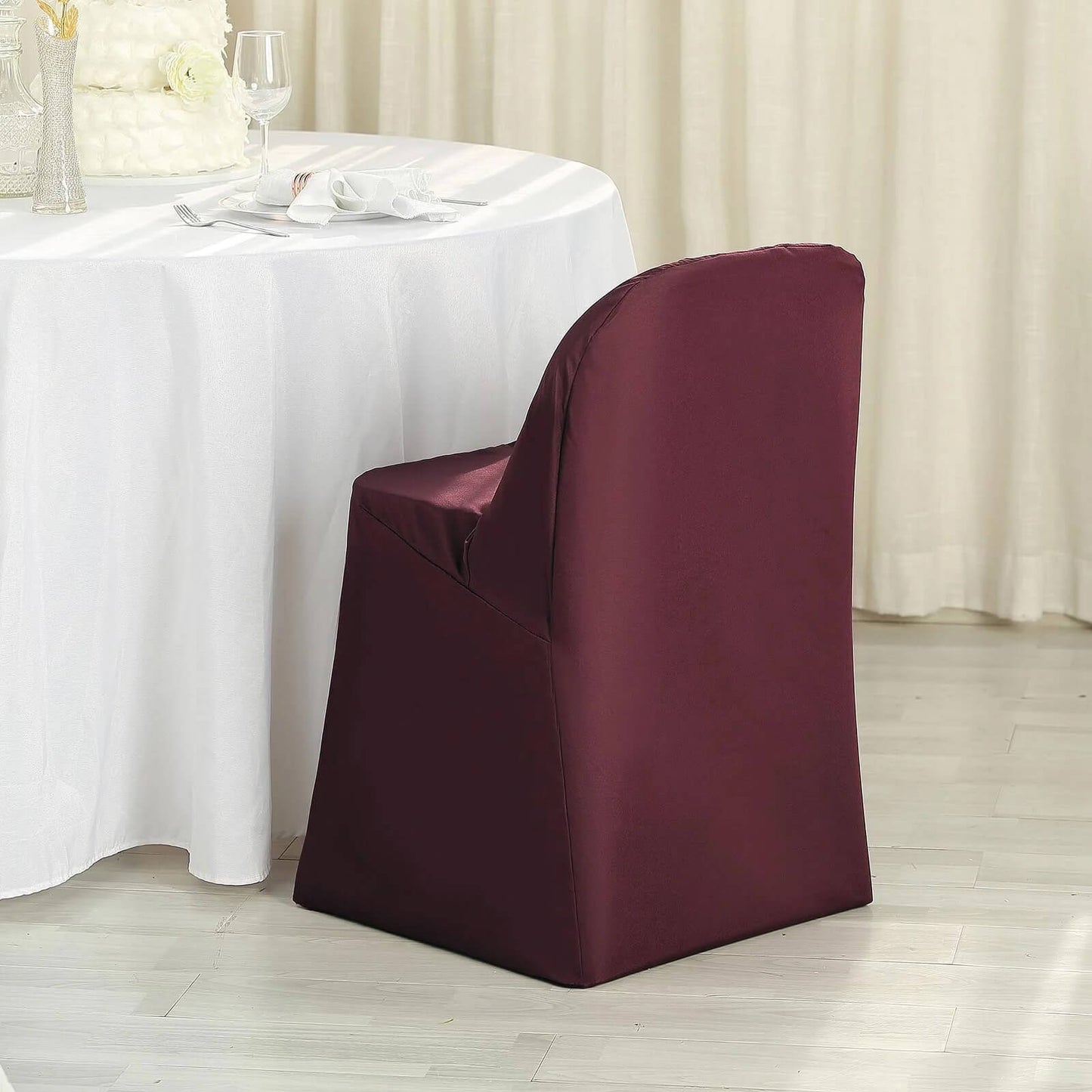 Burgundy polyester folding chair cover on a chair at a dining table.