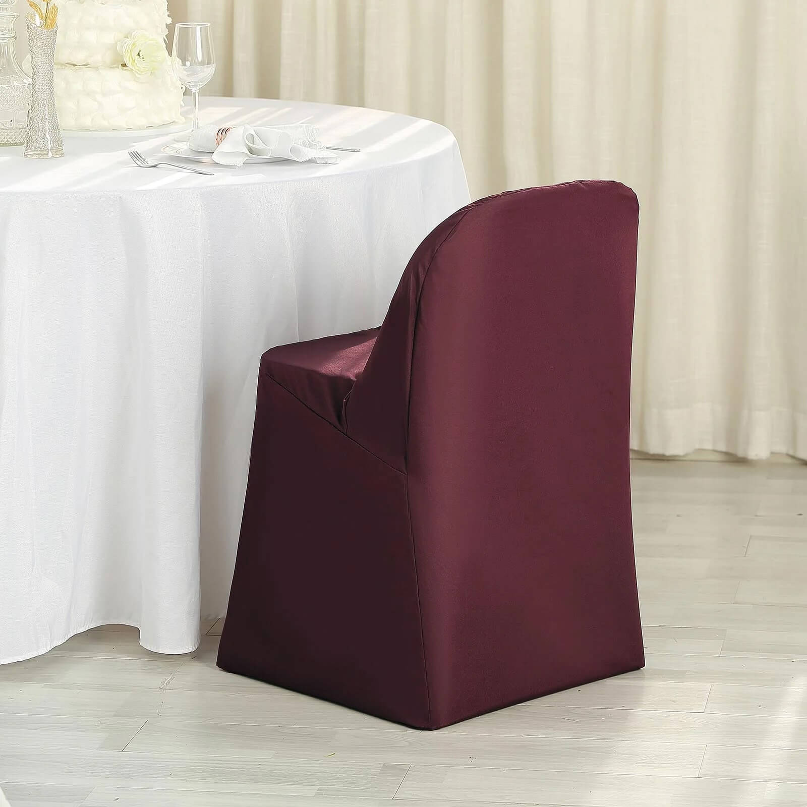 Burgundy polyester folding chair cover on a chair at a dining table.
