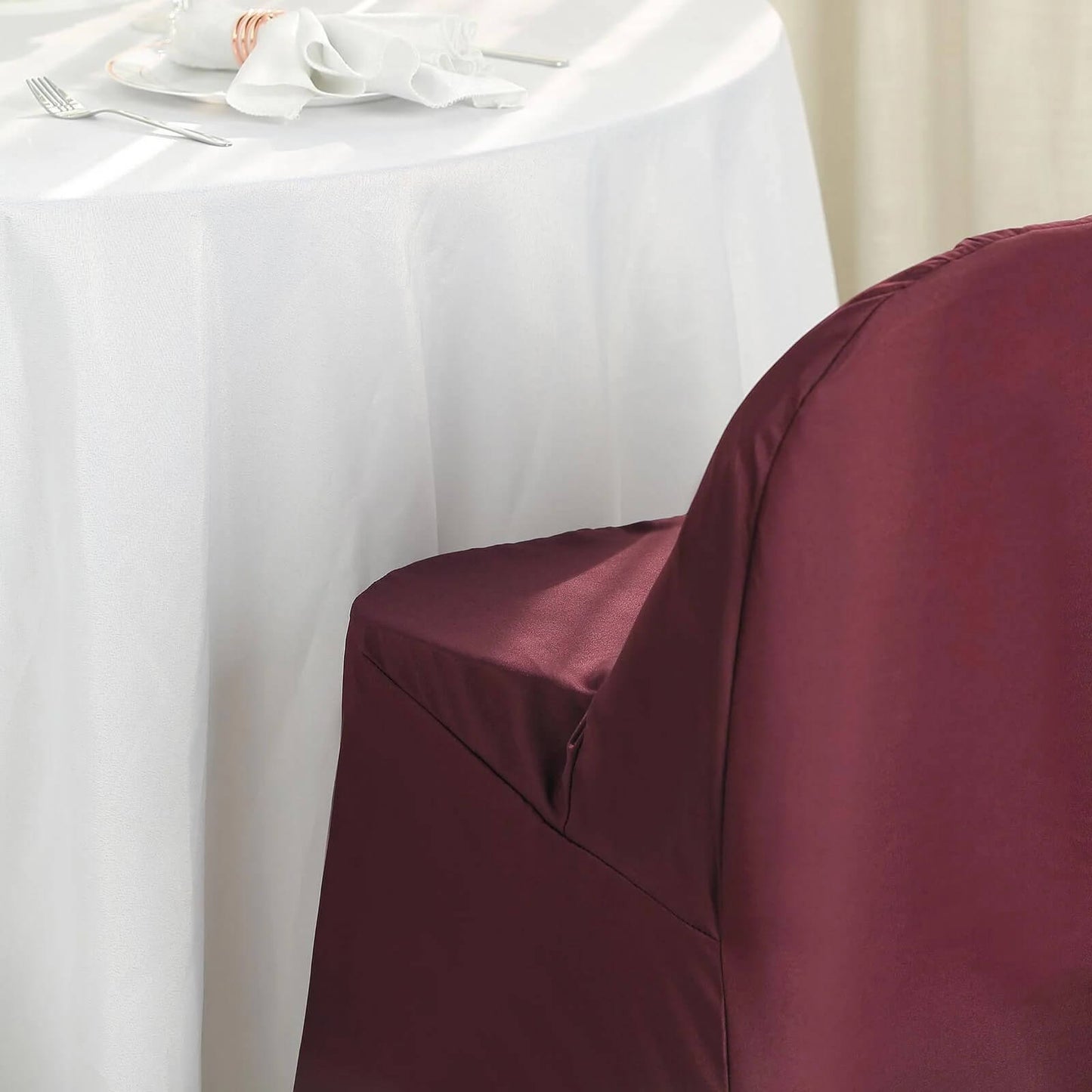 Burgundy polyester folding chair cover on a table setting.