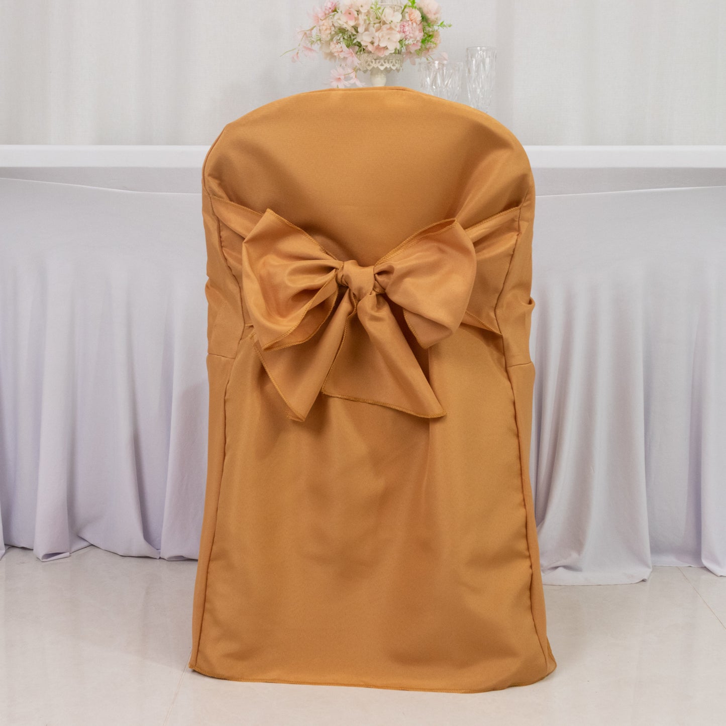Gold polyester slip-on folding chair cover with attached sash for events.