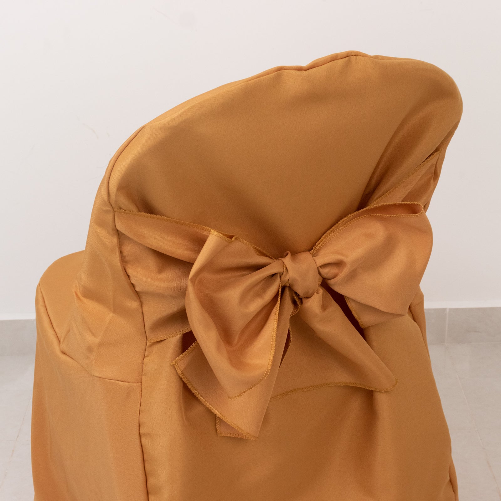 Gold slip-on folding chair cover with attached sash for events.