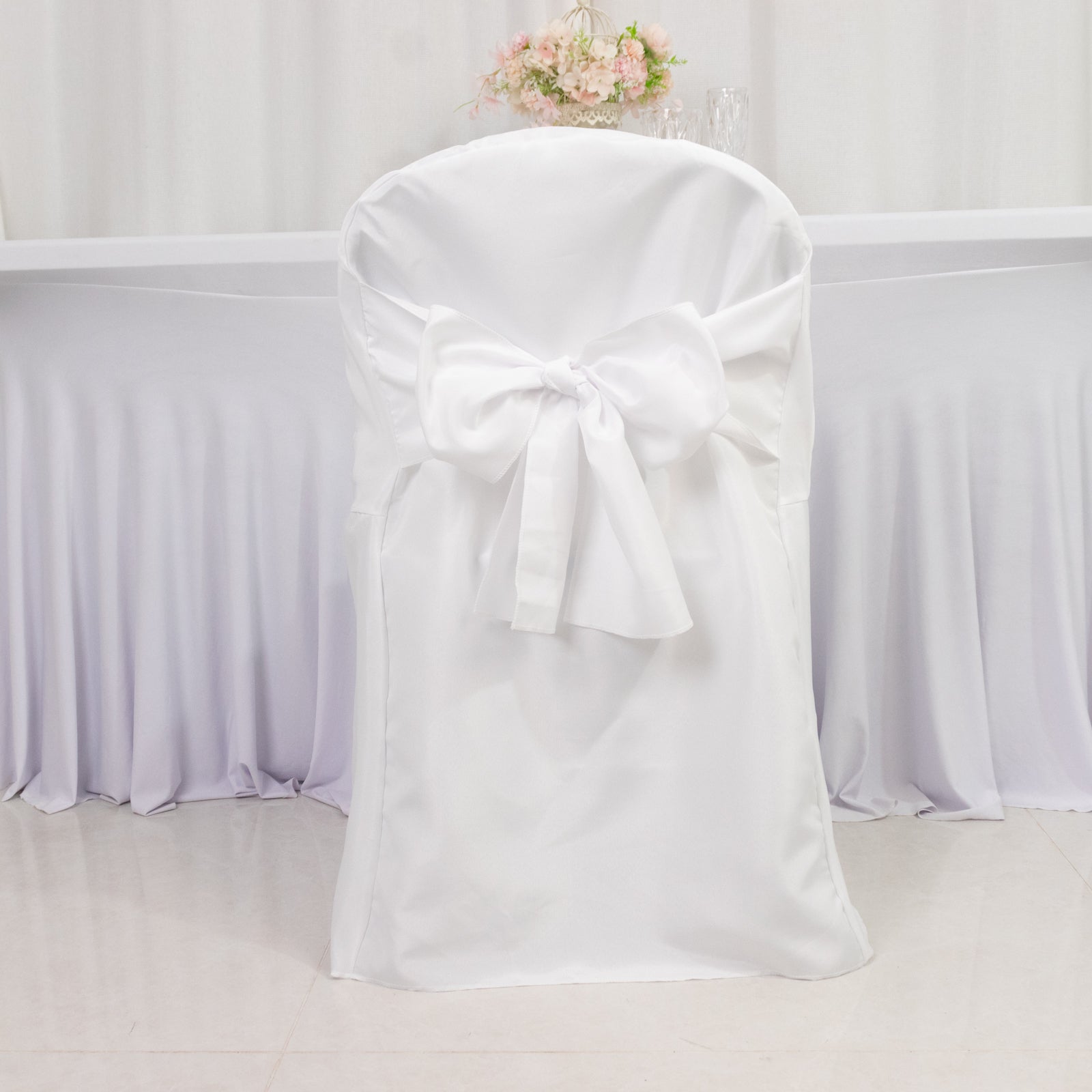White polyester slip-on folding chair cover with attached sashes.