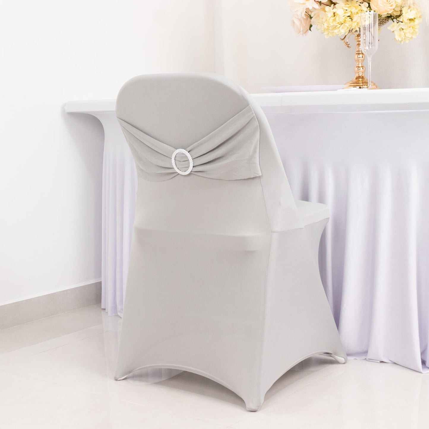 Silver spandex chair cover with rhinestone sash, fitted for elegance.