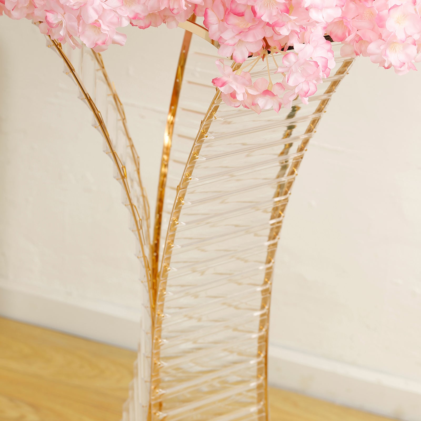 Gold metal hourglass flower stand with crystal details and pink floral arrangement.