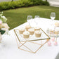 Gold geometric cake stand with square glass top displaying cupcakes.