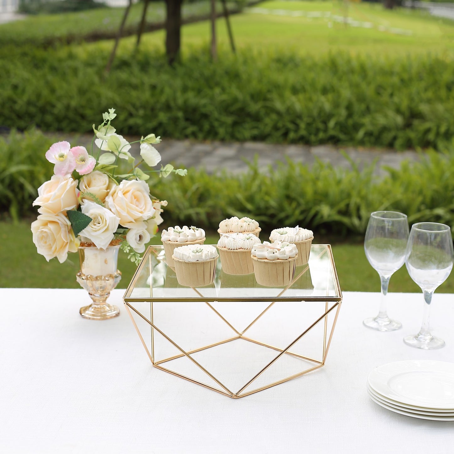 Gold geometric cake stand with square glass top displaying cupcakes.
