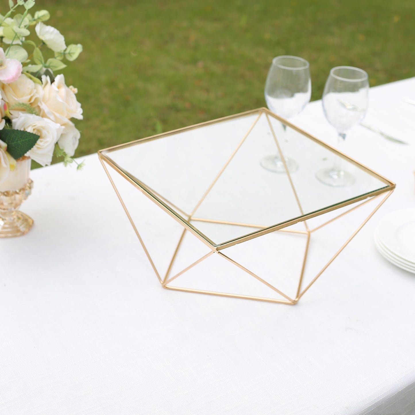 Gold geometric cake stand with square glass top on a table.