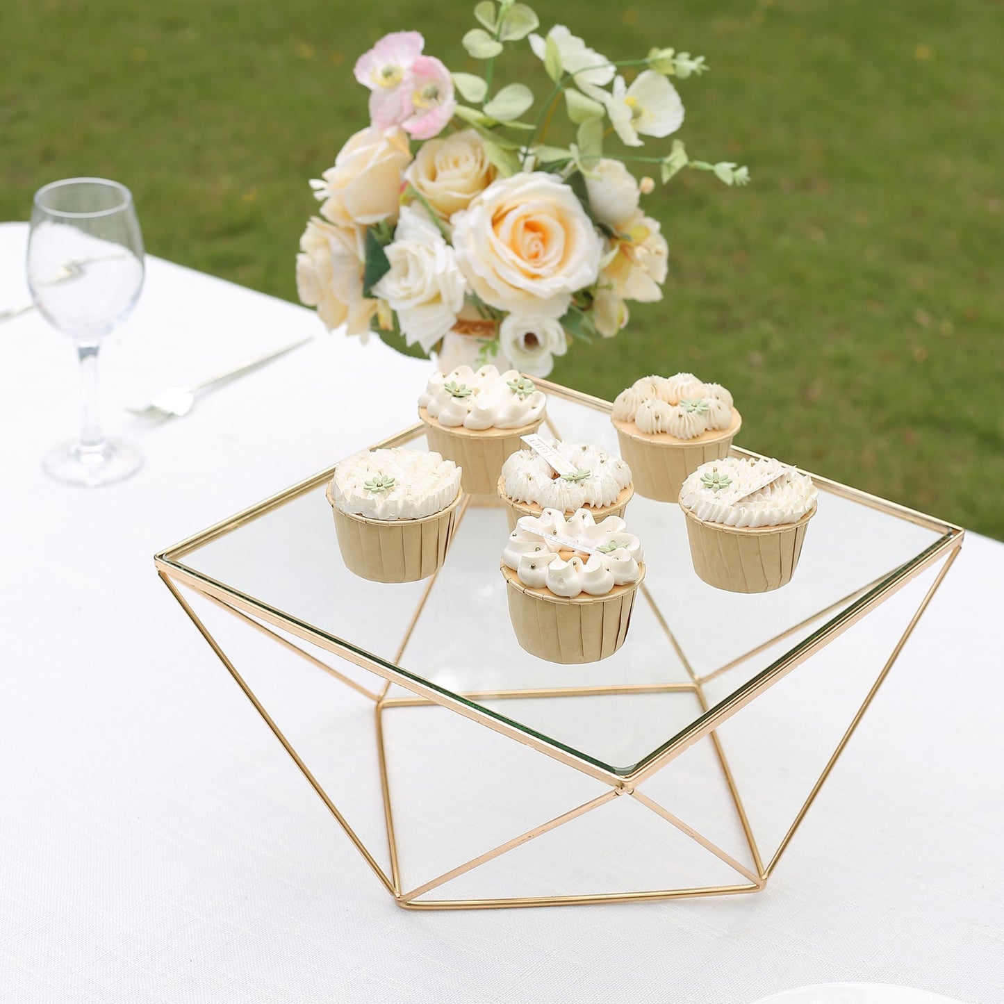 Gold metal geometric cake stand with glass top displaying cupcakes.