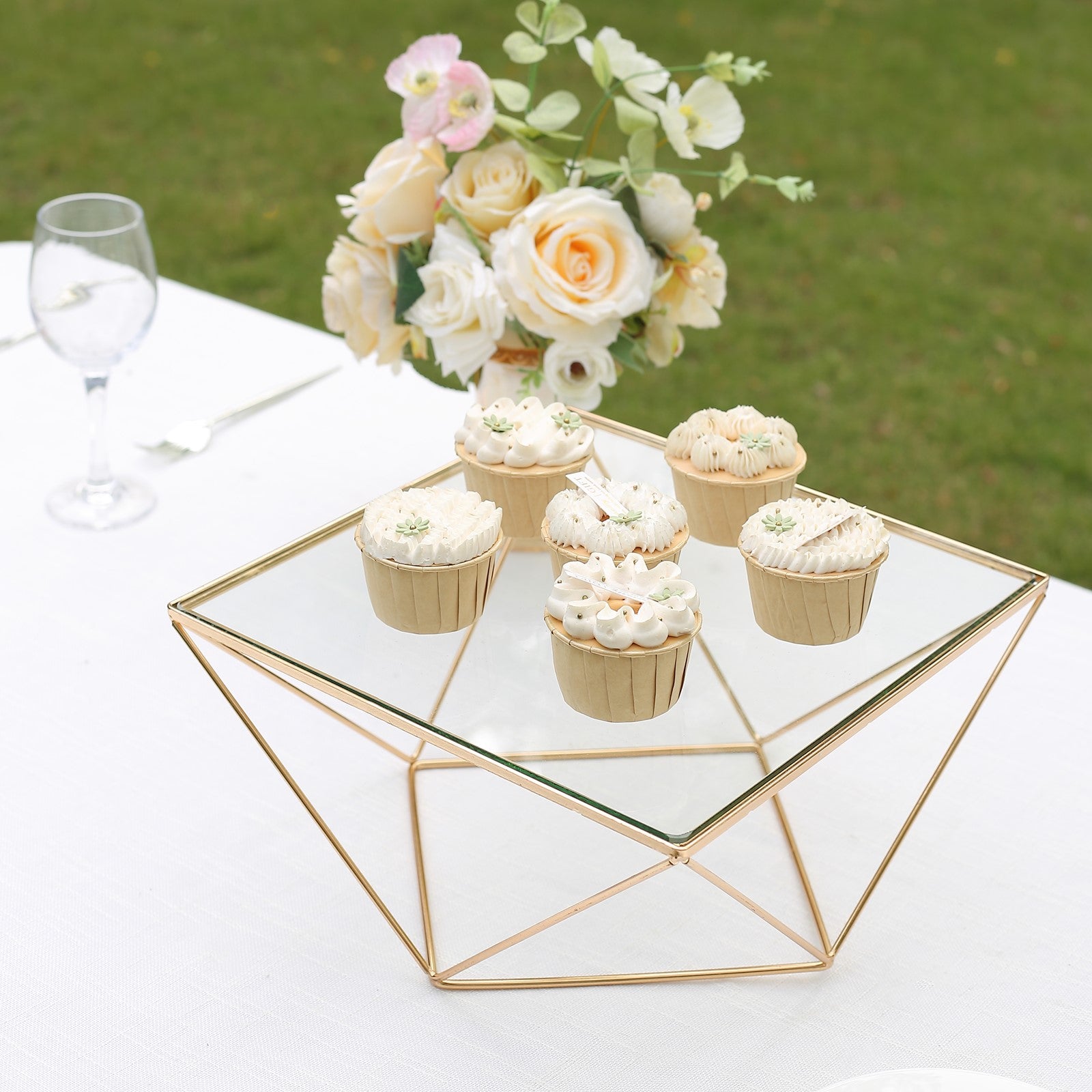 Gold metal geometric cake stand with glass top displaying cupcakes.