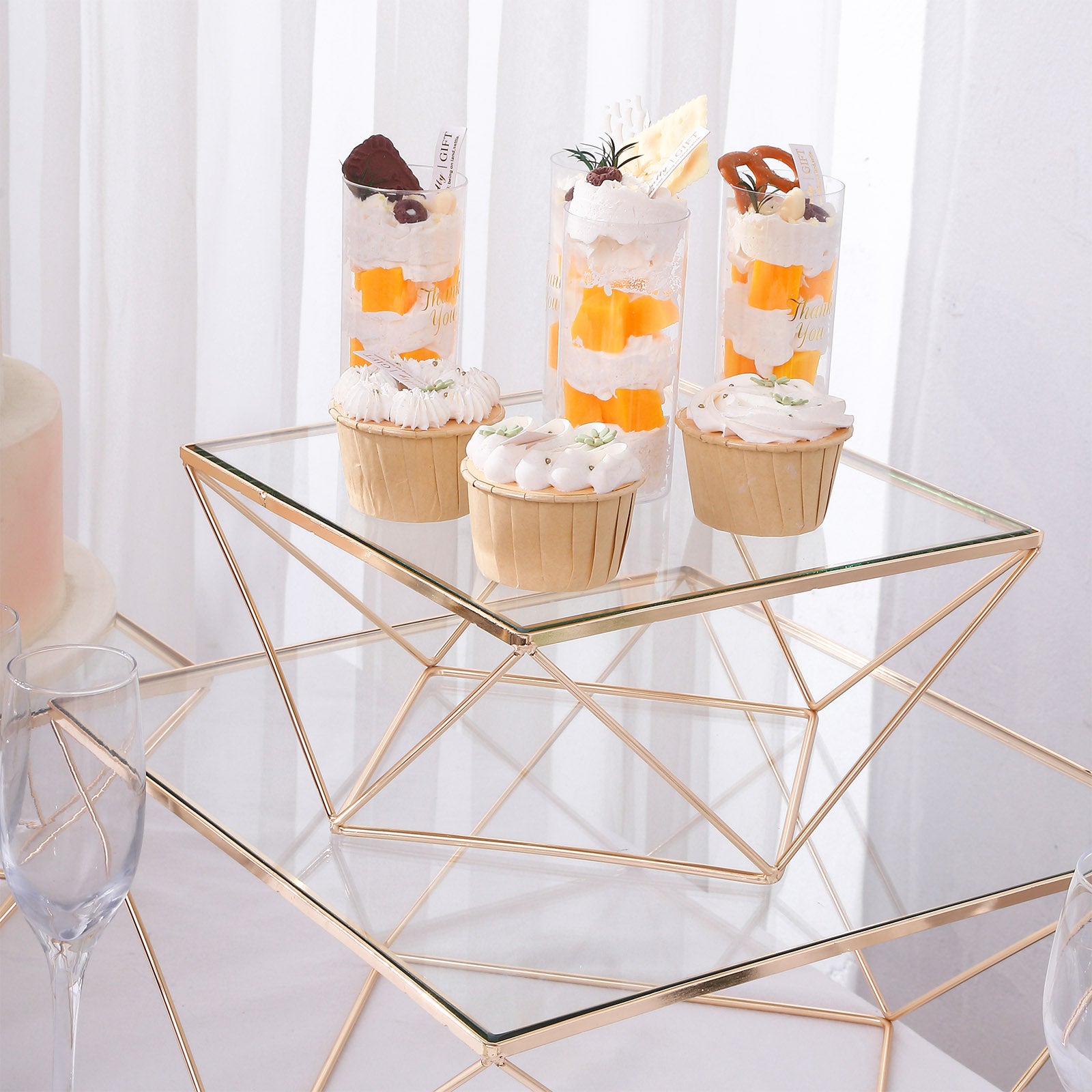 Gold metal geometric cake stand with square glass top displaying desserts.