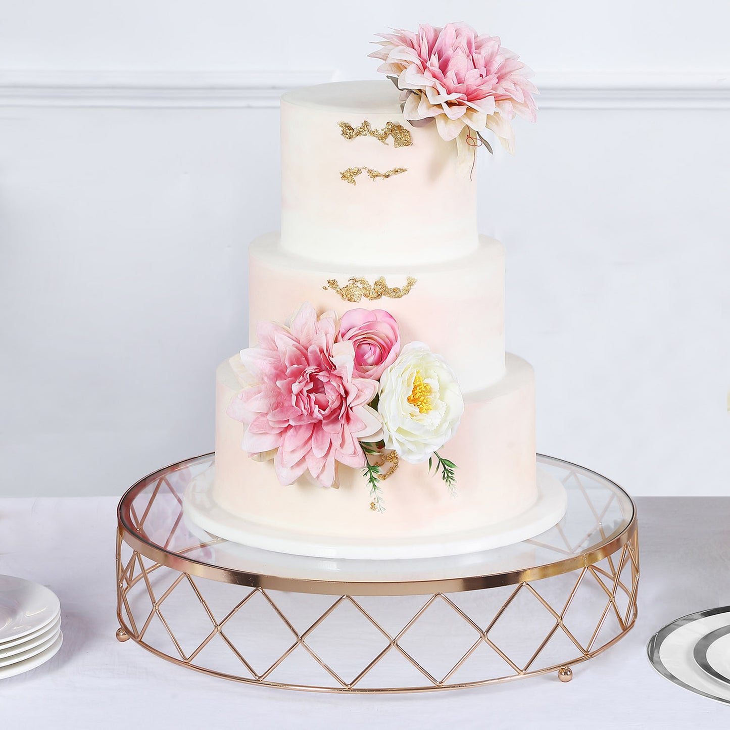 Gold geometric cake stand with glass top, featuring a three-tiered floral cake.