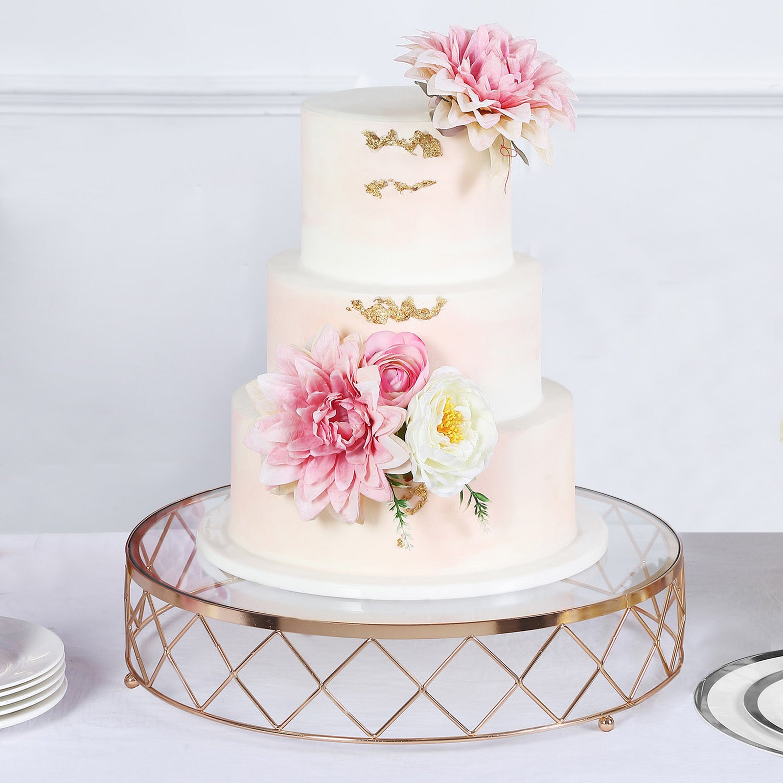 Gold geometric cake stand with glass top, featuring a three-tiered floral cake.