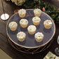 Gold metal geometric cake stand with glass top displaying decorative cupcakes.