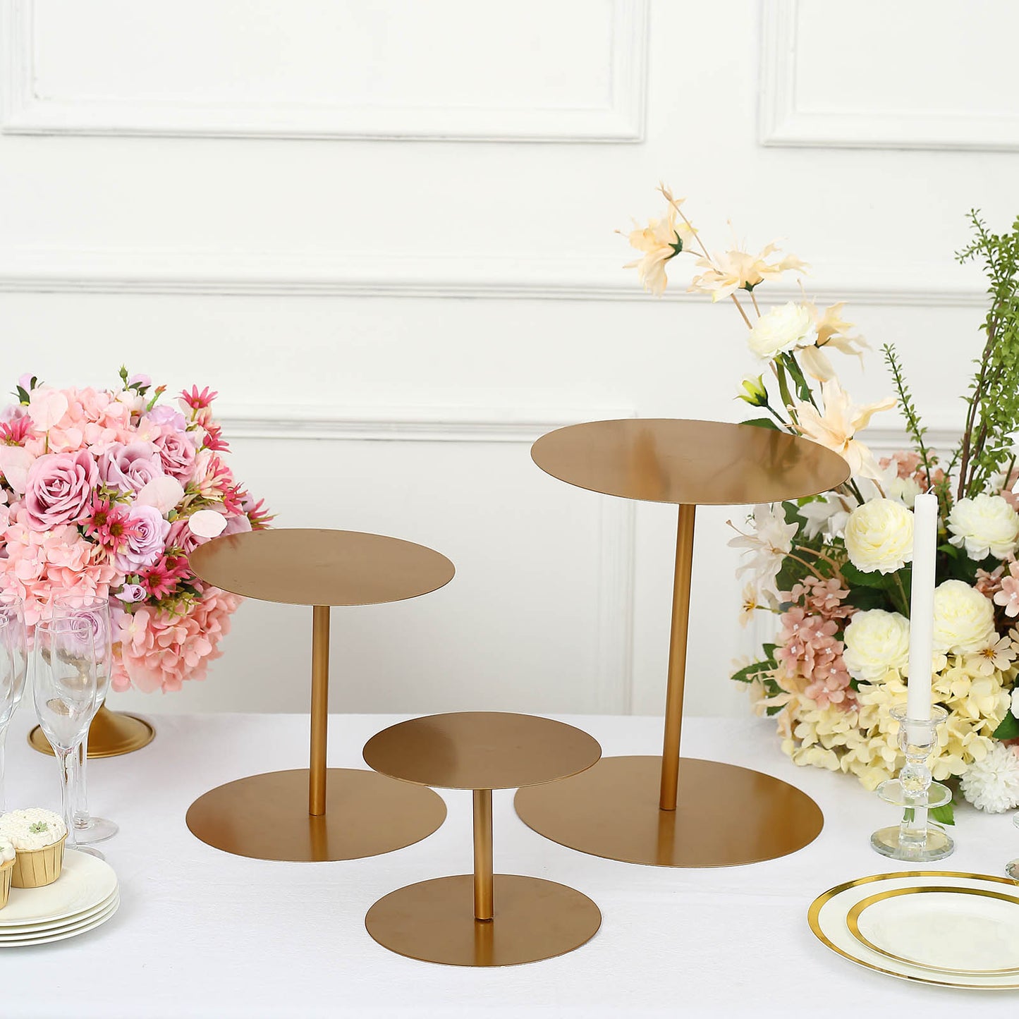 Gold metal round pedestal cupcake dessert stands in three sizes on a table.