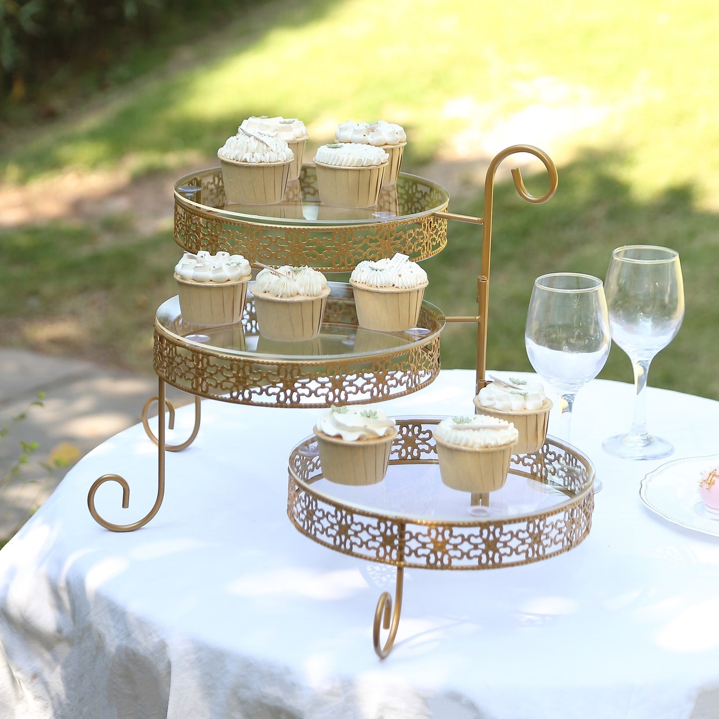 Gold metal rotating cake stand with clear acrylic plates and hollow lace design.