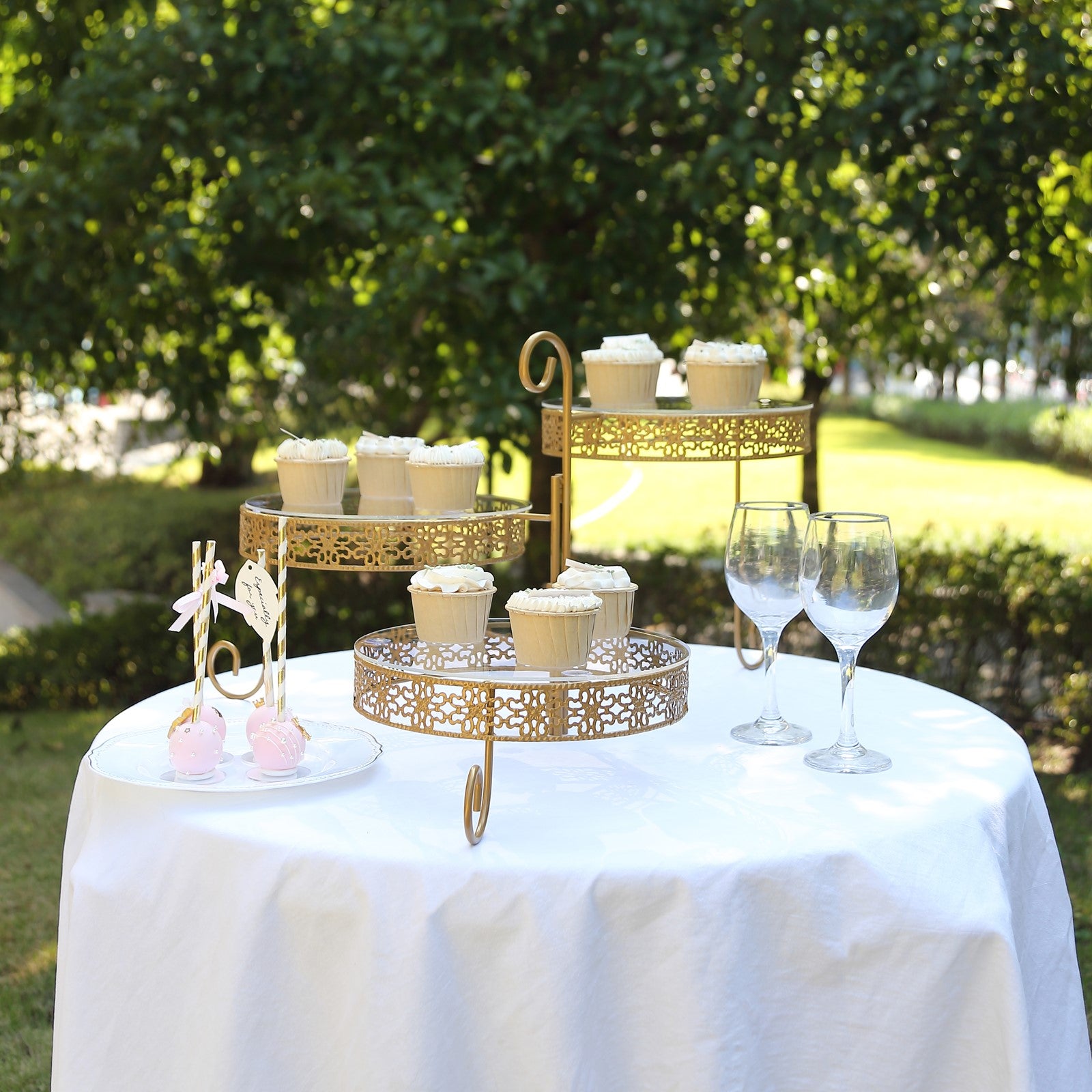 Gold metal rotating cake stand with clear acrylic plates displaying cupcakes outdoors.