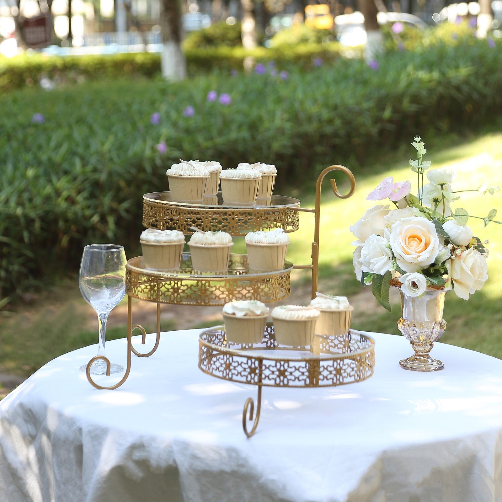 Gold metal rotating cake stand with clear acrylic plates and lace design, displaying cupcakes.