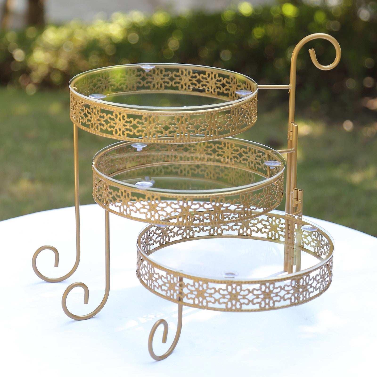 Gold metal rotating cake stand with clear acrylic plates and hollow lace design.