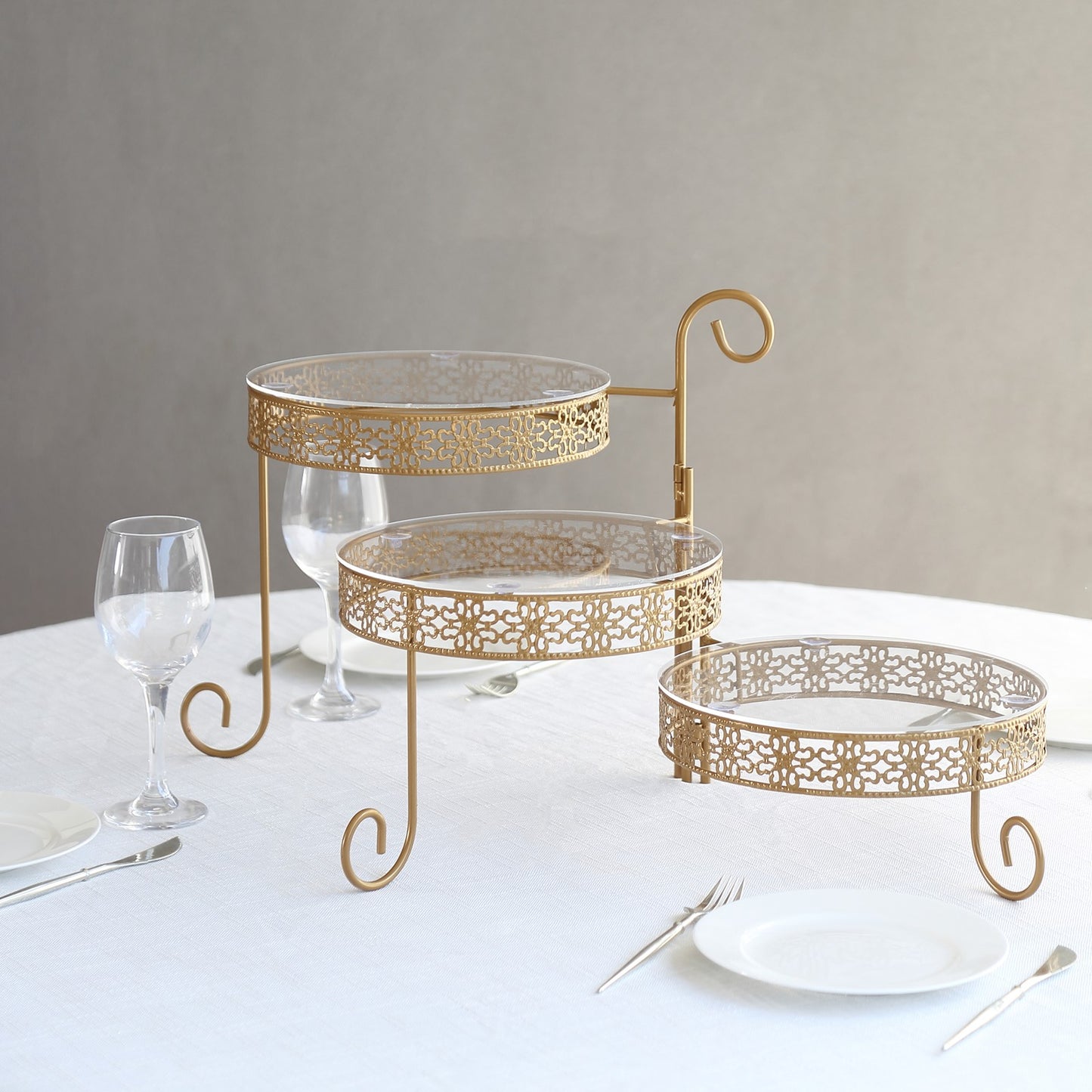 Gold metal rotating cake stand with clear acrylic plates and hollow lace design.