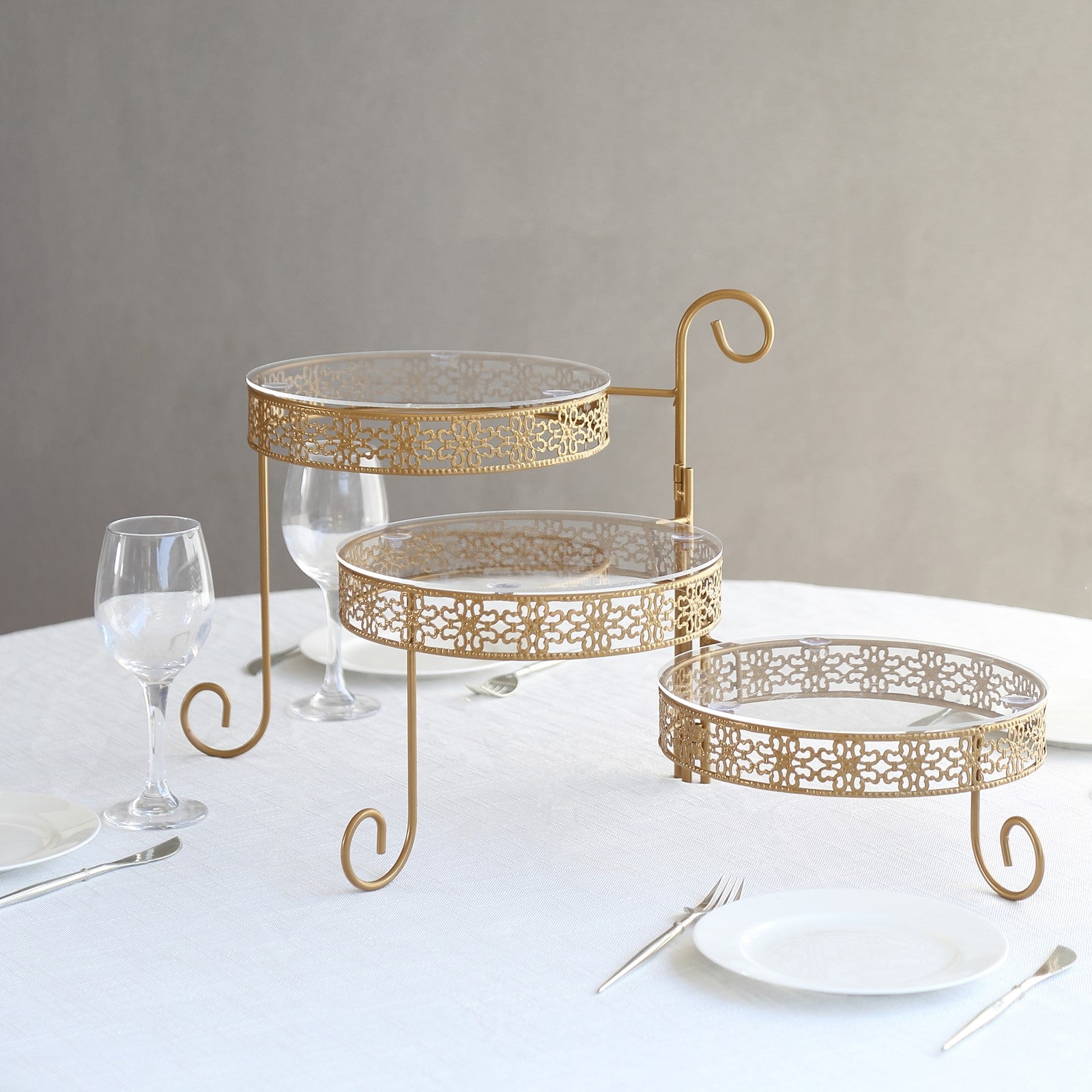 Gold metal rotating cake stand with clear acrylic plates and hollow lace design.