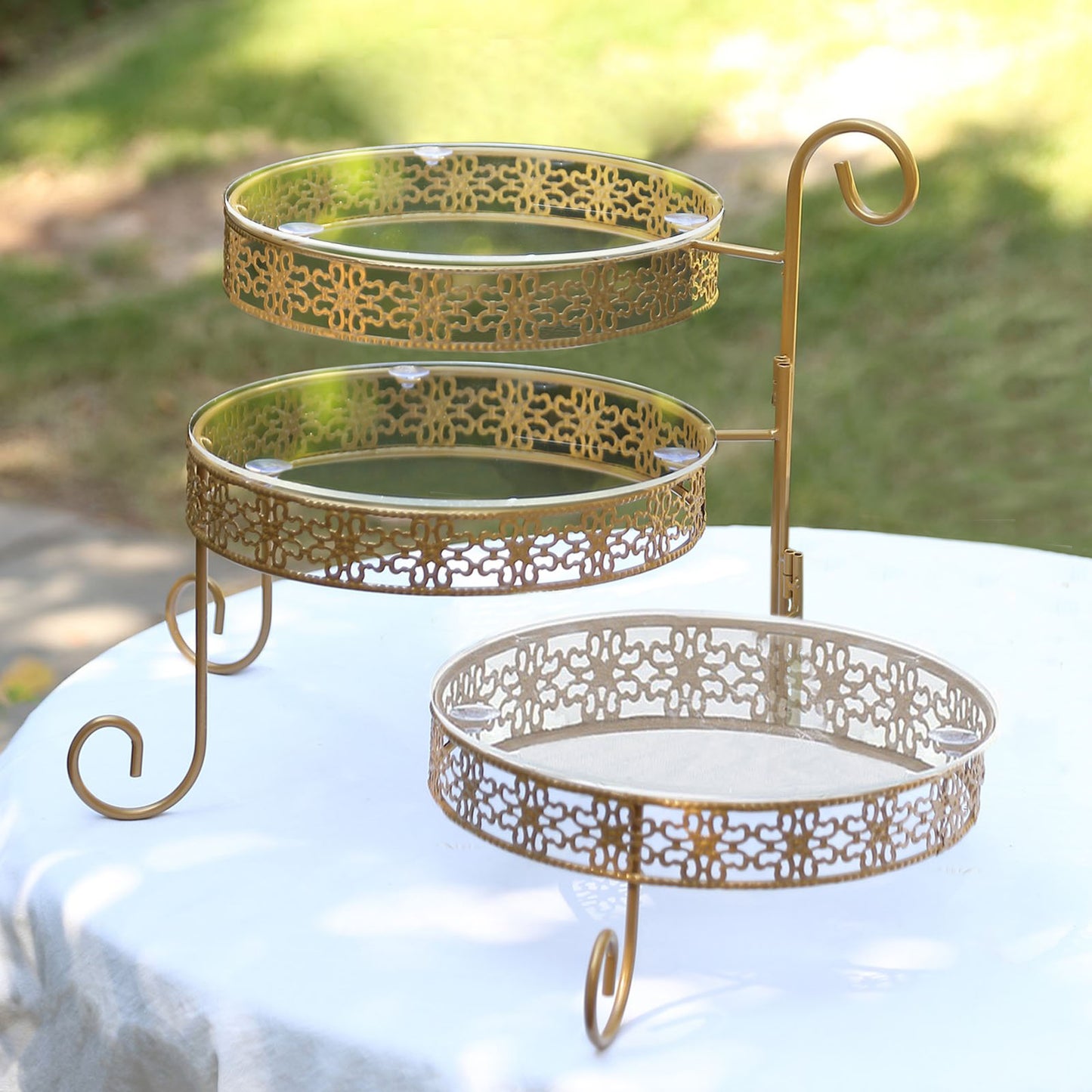 Gold metal rotating cake stand with clear acrylic plates and hollow lace design.