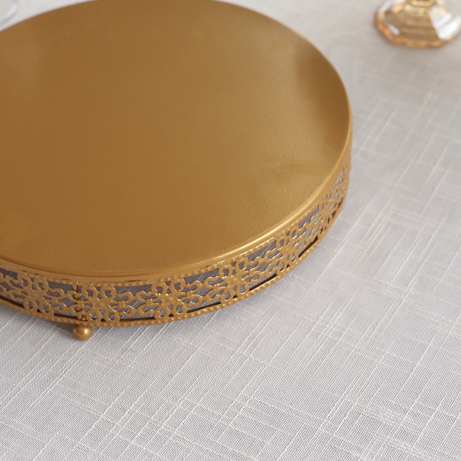 Gold metal round pedestal cake stand with decorative edge.