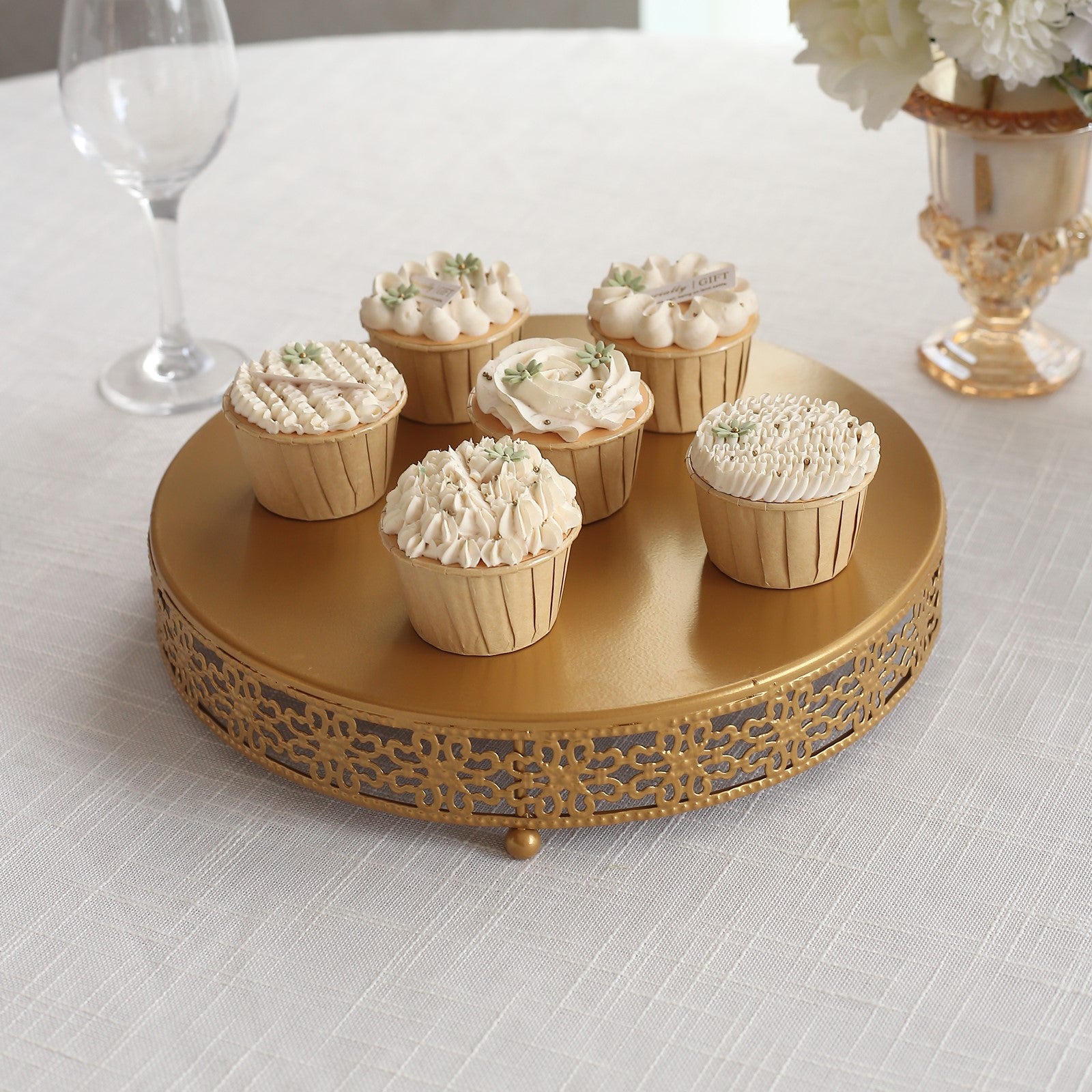Gold metal fleur de lis cupcake display stand with six decorated cupcakes.